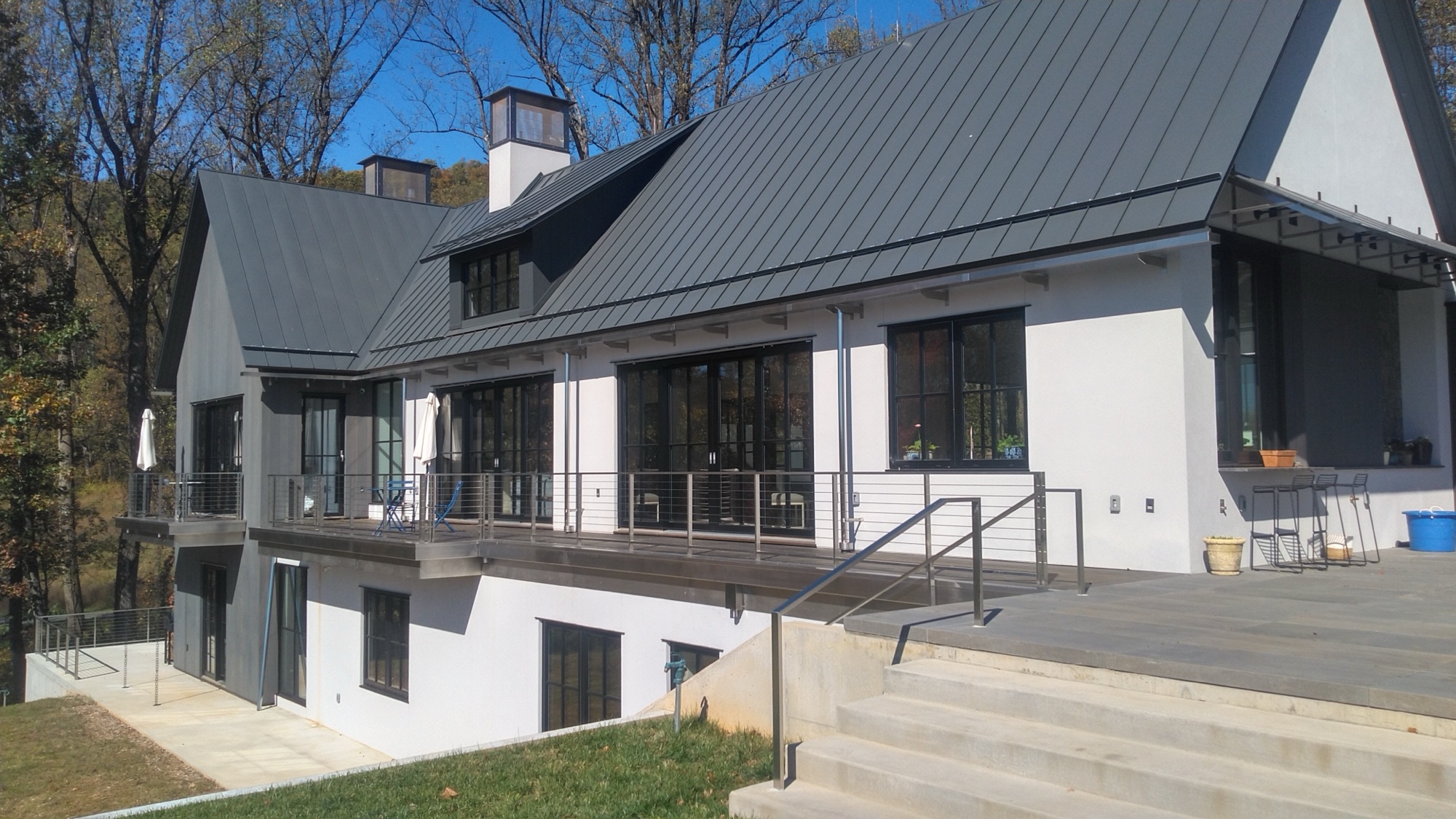 Modern white farmhouse exterior with brushed stainless cable railings across deck and second-story balcony