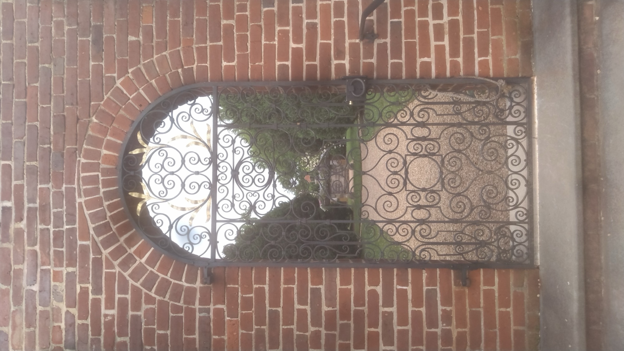Elaborate historic wrought iron gate with a golden sunburst detail set in a brick archway