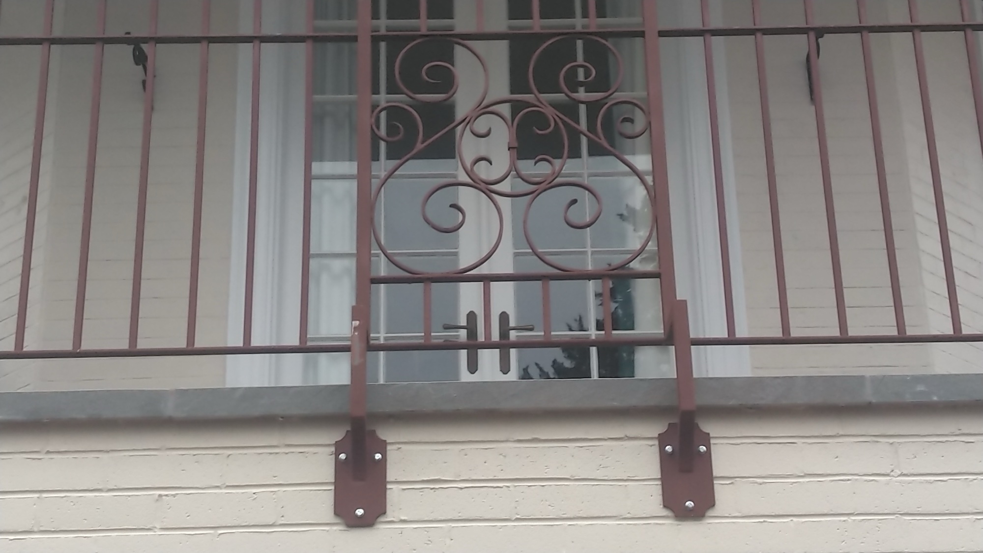 Closeup of the red-brown wrought iron S-monogram scrollwork on the mansion balcony